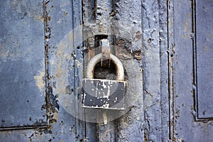 A blue old wooden door with a rusty steel lock. Farm gate from planks with an old padlock. The lock on the door