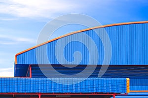 Blue and orange aluminium industrial factory building with louvered and dome roof against blue sky background