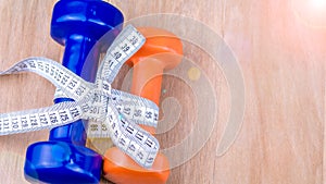 Blue and orange dumbbells bound together with centimetric tape as gift on wooden background photo
