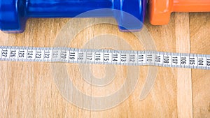 Blue and orange dumbbells and centimetric tape in front on wooden surface photo