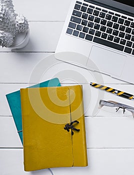 Blue and orange leather book, a pen, glasses and an open notebook on a white background of vintage wooden planks vertical top view