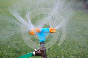 Blue and orange sprinkler watering grass. Garden irrigation system watering lawn. Closeup image of a garden sprinkler on