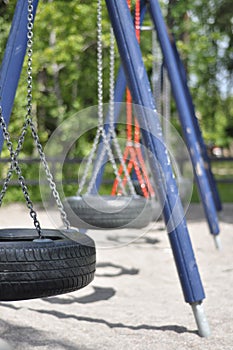 Blue and orange tyre swing set on a children\'s playground on sunny summer day. Tire swing with black tires, metallic chains