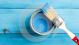 A blue paint can sits on a wooden surface with a paintbrush next to it. The blue paint is ready to be used for painting