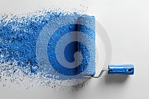 A blue paint roller is on a white surface with blue paint
