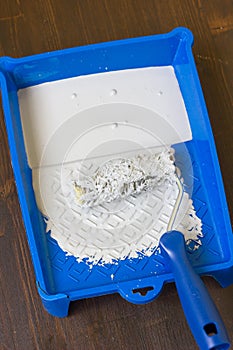 Blue paint tray with paint roller and paint inside it.