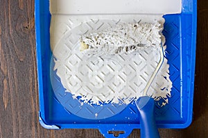 Blue paint tray with paint roller and paint inside it.