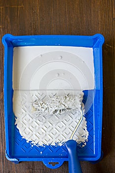 Blue paint tray with paint roller and paint inside it.