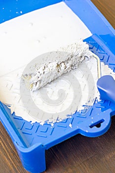 Blue paint tray with paint roller and paint inside it.