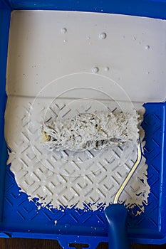 Blue paint tray with paint roller and paint inside it.