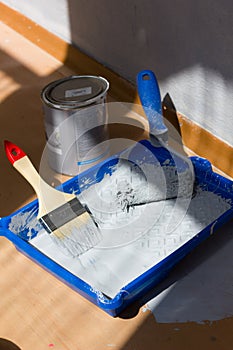 Blue paint tray with paint roller and brush inside it.