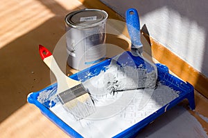 Blue paint tray with paint roller and brush inside it.
