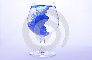 Blue paint in water in a crystal glass on a white background