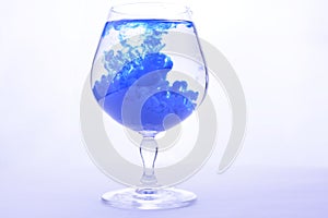 Blue paint in water in a crystal glass on a white background