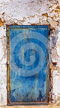 Blue painted metal door with drilled flower pattern. Rusty, stained and with fingerprints. Orange, blue, yellow. Scratched and de