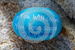 Blue painted rock stating You WIN some You Lose some Try try again