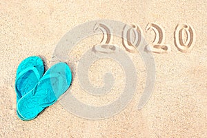 Blue pair of flip flops on the beach, 2020 written in the sand. Tropical new year holiday card