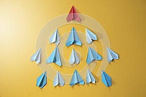 Blue paper aeroplane origami following rhe red one on yellow background