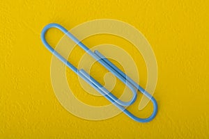 Blue paper clip isolated on a yellow background