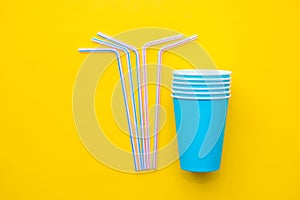 Blue paper cups with drinking colored plastic straws on yellow background. Set for party. Top view. Minimalist Style. Copy, empty