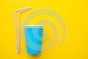 Blue paper cups with drinking colored plastic straws on yellow background. Set for party. Top view. Minimalist Style. Copy, empty