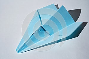 Blue paper plane lying on white background with hard shadows.