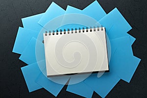 Blue paper stickers and notepad or book in middle on black background. Sticky notes blank with copy space ready for your message.