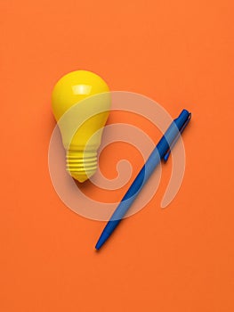 A blue pen and a bright yellow light bulb on an orange background. Flat lay