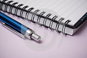 blue pen and spirales notebook on purple background