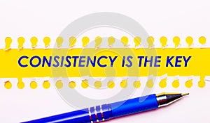 Blue pen and white torn paper stripes on a bright yellow background with the text CONSISTENCY IS THE KEY