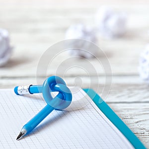 Blue Pencil with knot on writing pad on white wood background
