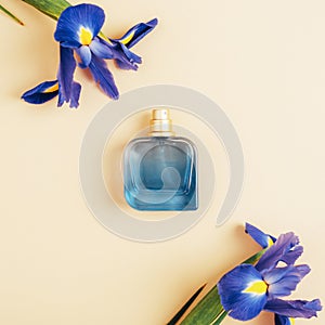 Blue perfume bottle and iris flowers on light background. Top view, flat lay, mockup