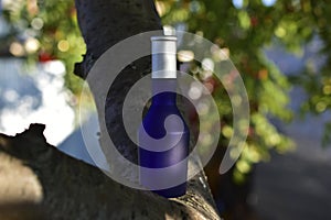 Blue perfume bottle with a white lid on a background of flowers and mountain ash