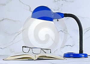 A blue personal sized desk lamp on a marble desk in front of a marble