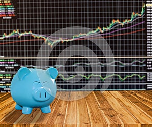 blue pig bank on wood background with blur stock market background,money and saving concept.