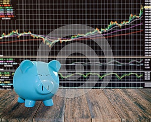 blue pig bank on wood background with blur stock market background,money and saving concept.