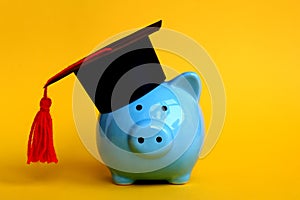 Blue pig piggy bank stands in a black school hat on a yellow background