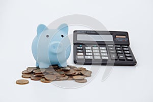 Blue piggy or coin bank or piggybank or money box on coins and calculator - finance and savings concept on white