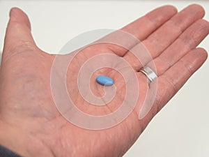 Blue pill for treating erectile dysfunction or impotence. One single pill held in palm of hand. photo