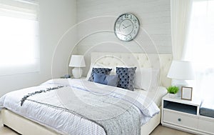 Blue pillow on bed with side table lamp and large clock on wall in bedroom