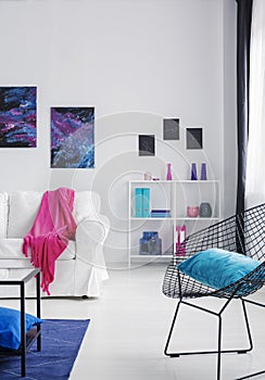 Blue pillow on black stylish metal armchair in bright cosmos inspired interior with white furniture, real photo with copy space on