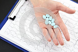 Blue pills in hand and medical questionnaire form on background