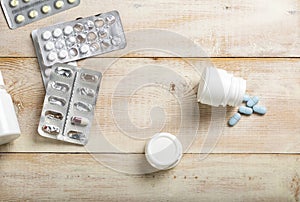 Blue pills spilled from a white plastic bottle. Different drug boxes and bottles in the background.