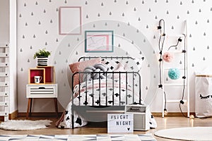 Blue and pink pompons and lights on wooden white scandinavian ladder in stylish bedroom interior with black and white bedding, photo