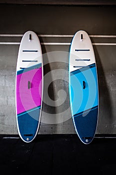 Blue and pink stand-up paddle boards SUP by the wall. Surfing and sup boarding equipment close up photo