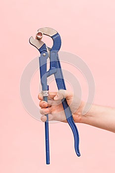 Blue pipe adjustable pipe gas plumbing wrench in a male hand close-up on a pink background