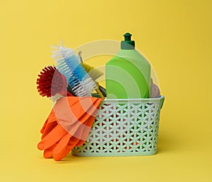 Blue plastic basket with brushes, sponges and rubber gloves for cleaning, yellow background