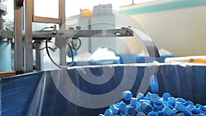 Blue plastic bottle caps fall from conveyor to the