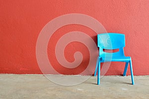 Blue plastic chair laid against the red wall. Copy space for the text