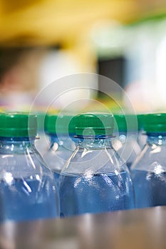 Blue plastic half-liter small volume water bottles with green cap lid in store, supermarket shelf, close up.